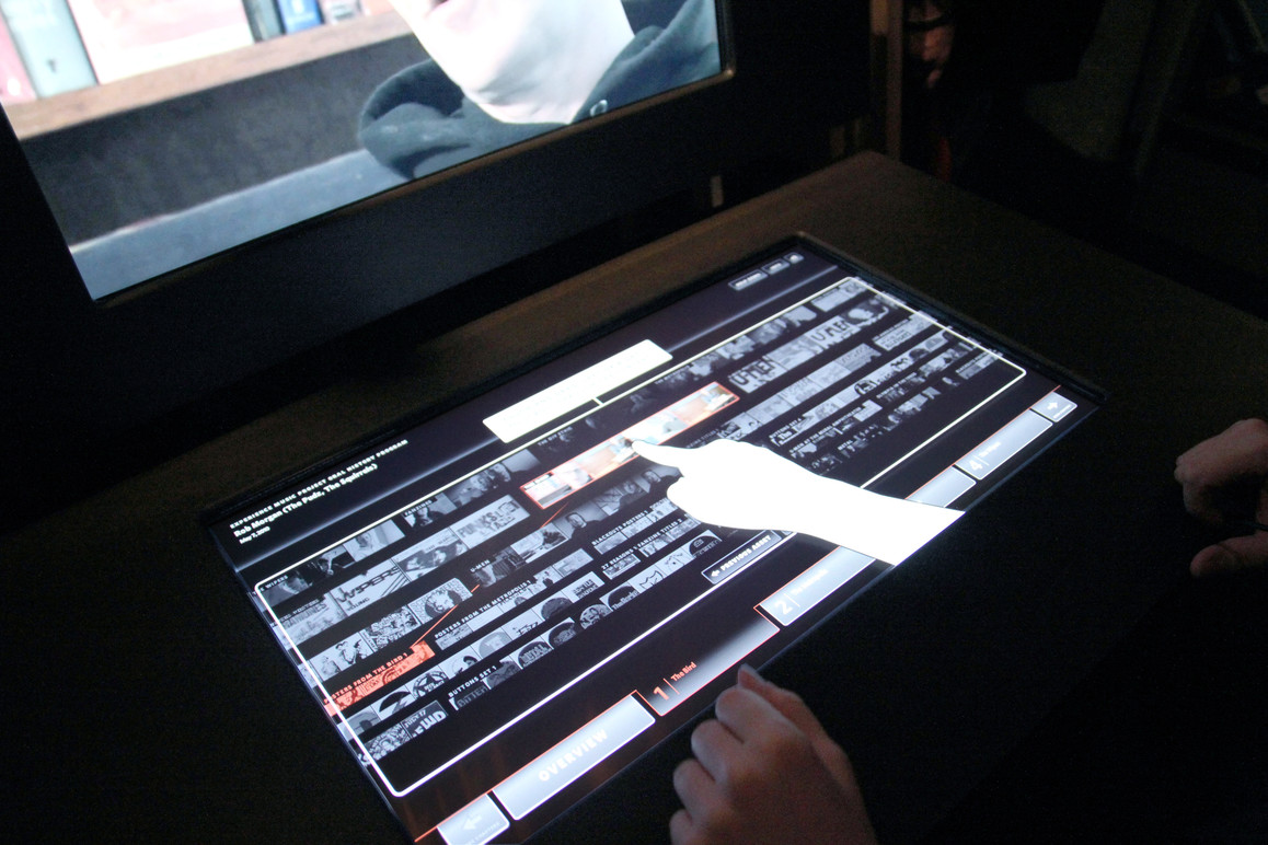 Touchtable help mode. A hand appears showing the user how to interact with the kiosk.