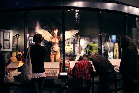 Visitors looking at objects in the long display case with photo murals behind them.